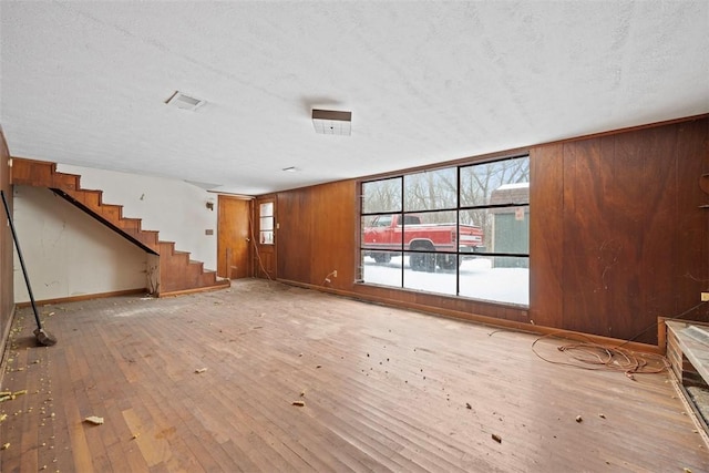 unfurnished living room featuring hardwood / wood-style floors, a textured ceiling, and wood walls