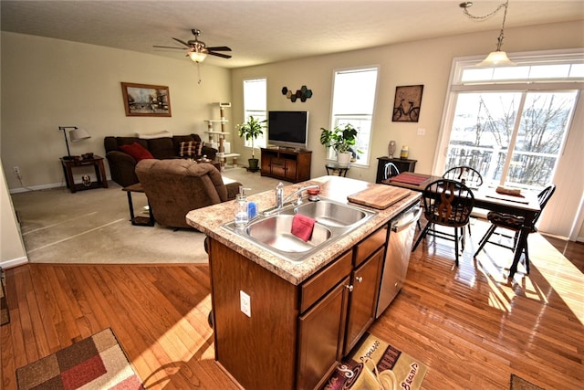 kitchen featuring pendant lighting, dishwasher, sink, a kitchen island with sink, and light hardwood / wood-style flooring