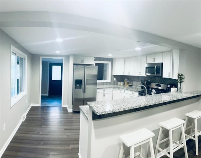 kitchen featuring white cabinetry, a kitchen breakfast bar, stainless steel appliances, decorative backsplash, and kitchen peninsula