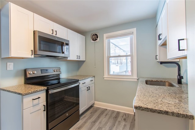 kitchen with white cabinetry, stainless steel appliances, light stone countertops, and sink