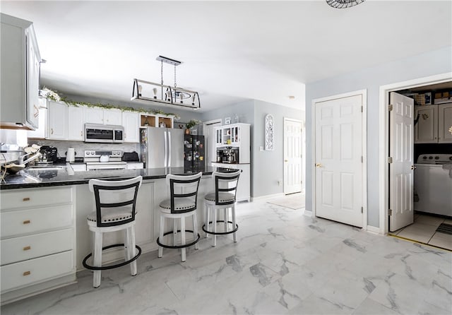 kitchen with appliances with stainless steel finishes, white cabinetry, hanging light fixtures, a kitchen bar, and washer / dryer