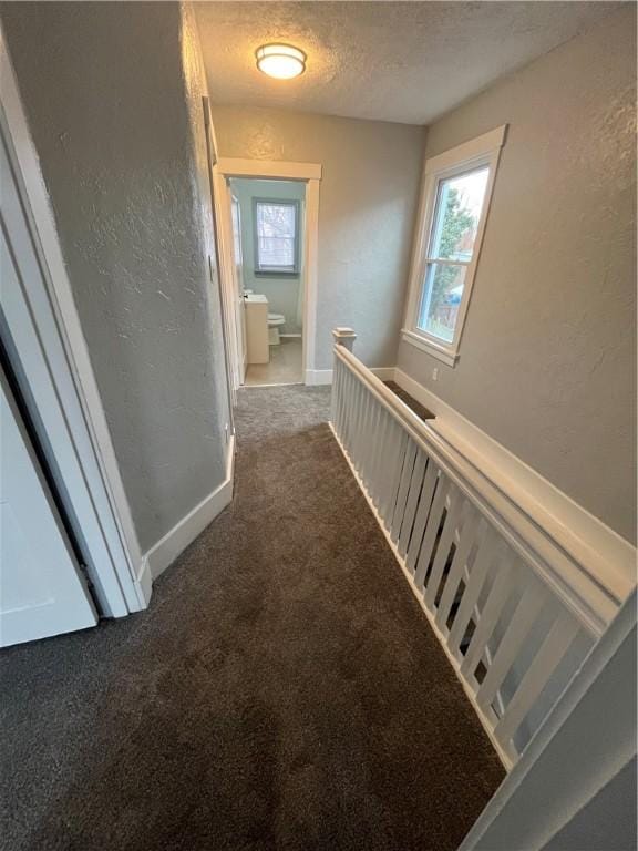 corridor featuring a textured ceiling and dark carpet