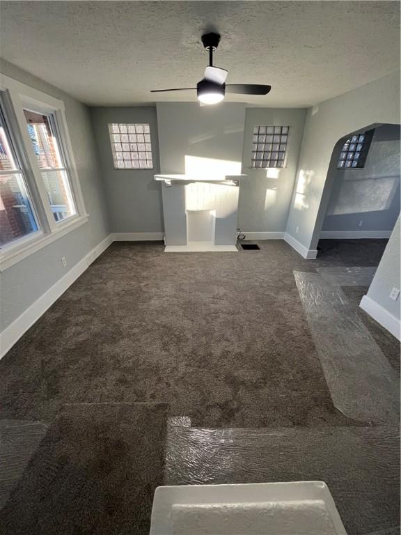 unfurnished living room featuring ceiling fan, dark carpet, and a textured ceiling