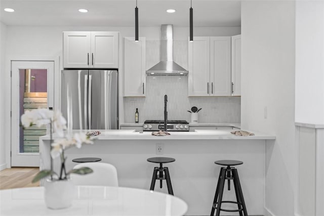 kitchen featuring a kitchen breakfast bar, white cabinetry, stainless steel refrigerator, and wall chimney exhaust hood