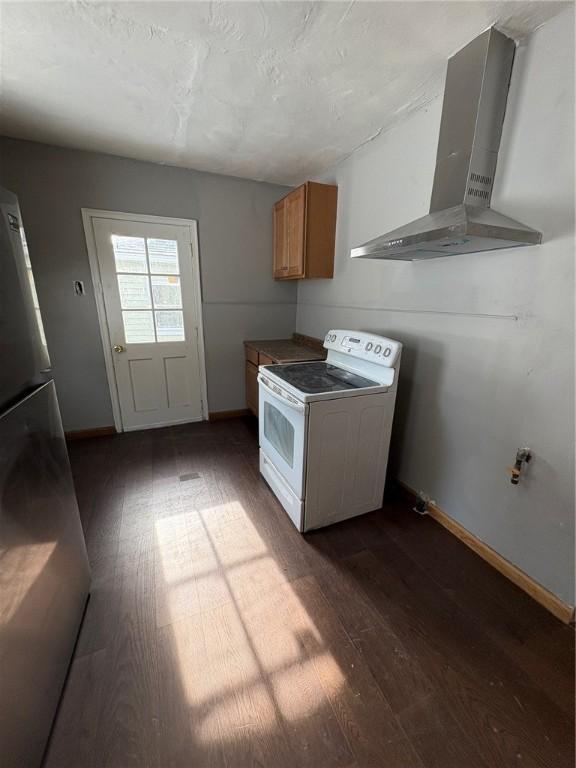 kitchen featuring wall chimney range hood, electric range, dark wood-type flooring, and stainless steel refrigerator