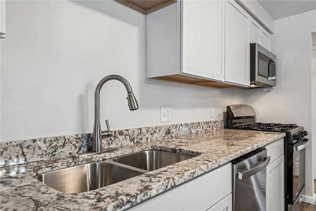 kitchen featuring stainless steel appliances, white cabinetry, light stone countertops, and sink