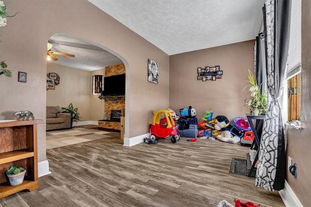 interior space with lofted ceiling, ceiling fan, hardwood / wood-style floors, a large fireplace, and a textured ceiling