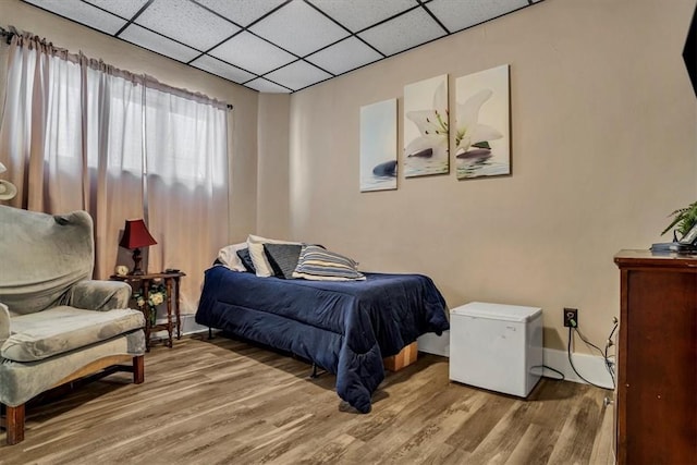 bedroom featuring hardwood / wood-style flooring, a paneled ceiling, and fridge