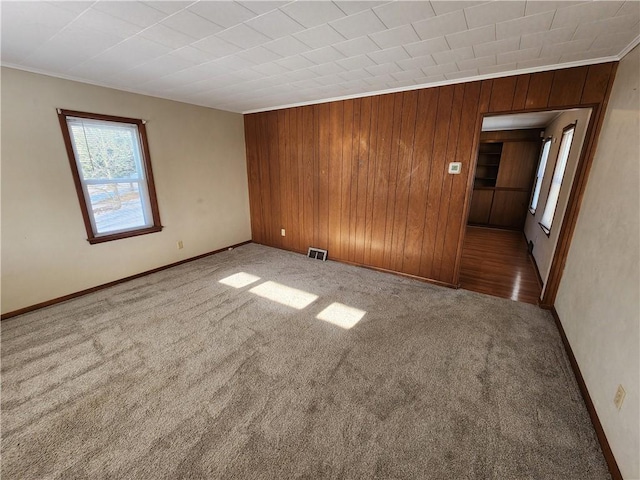 carpeted spare room featuring ornamental molding and wood walls