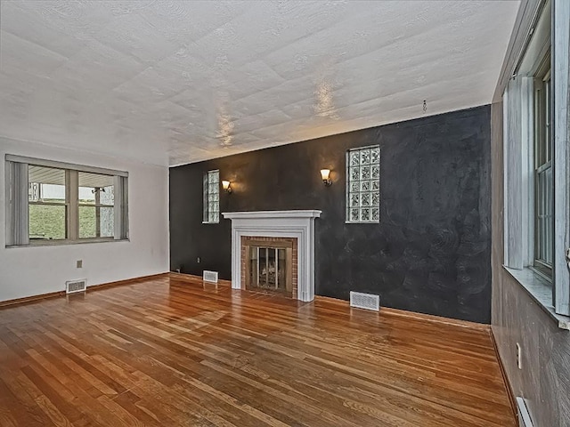 unfurnished living room featuring wood-type flooring, a fireplace, and a baseboard heating unit