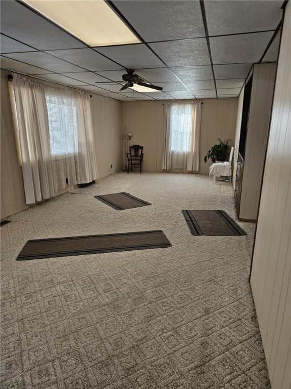 interior space featuring a drop ceiling, ceiling fan, and wood walls