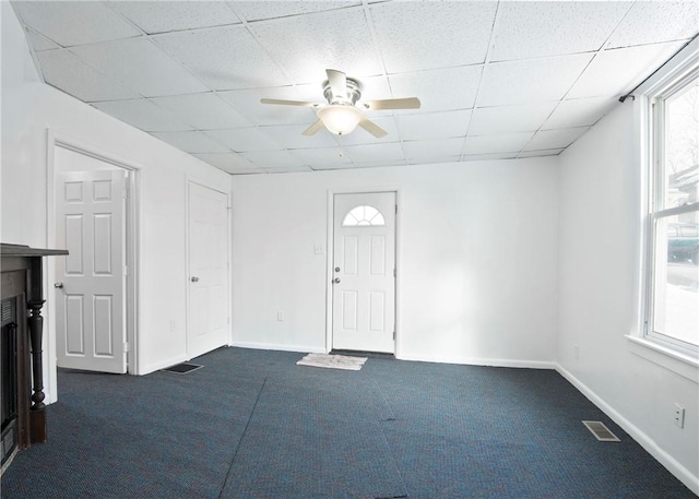 interior space with ceiling fan, dark carpet, and a drop ceiling