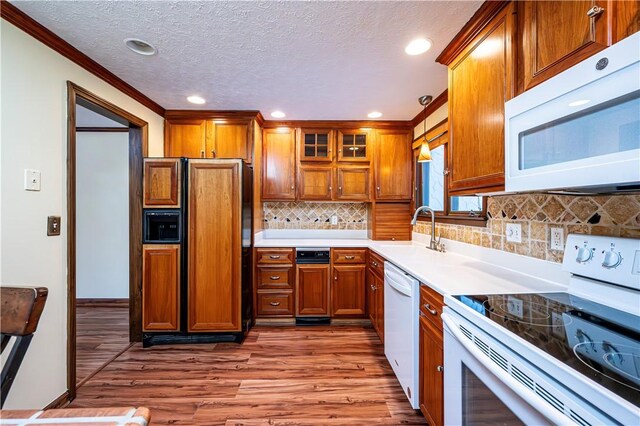 kitchen with sink, backsplash, hanging light fixtures, white appliances, and light hardwood / wood-style flooring