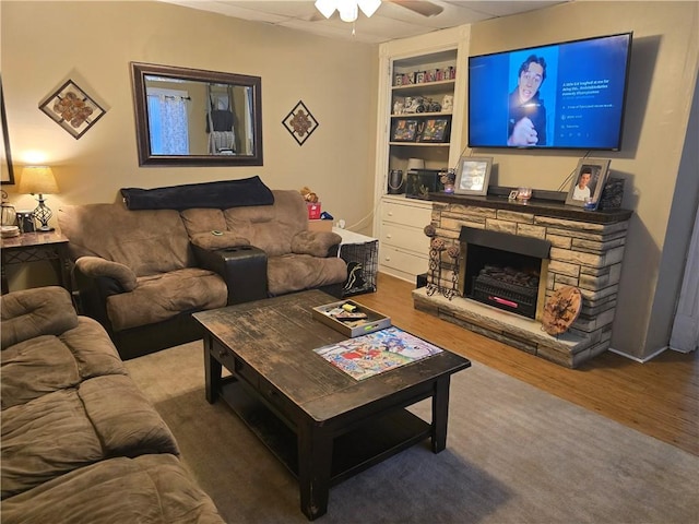 living room featuring built in shelves, ceiling fan, a stone fireplace, and hardwood / wood-style flooring