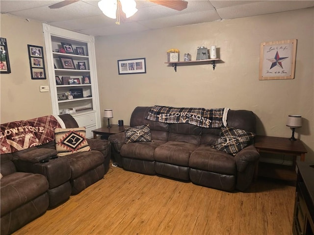 living room featuring ceiling fan, a drop ceiling, and light wood-type flooring