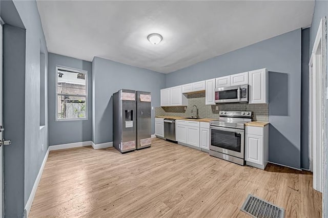 kitchen with sink, tasteful backsplash, light hardwood / wood-style flooring, stainless steel appliances, and white cabinets