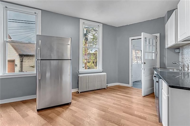 kitchen with sink, white cabinetry, stainless steel refrigerator, radiator heating unit, and light hardwood / wood-style floors