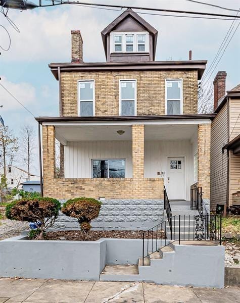 american foursquare style home featuring board and batten siding, brick siding, covered porch, and a chimney