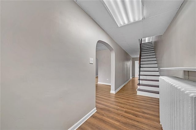 hallway with stairway, radiator, wood finished floors, baseboards, and arched walkways