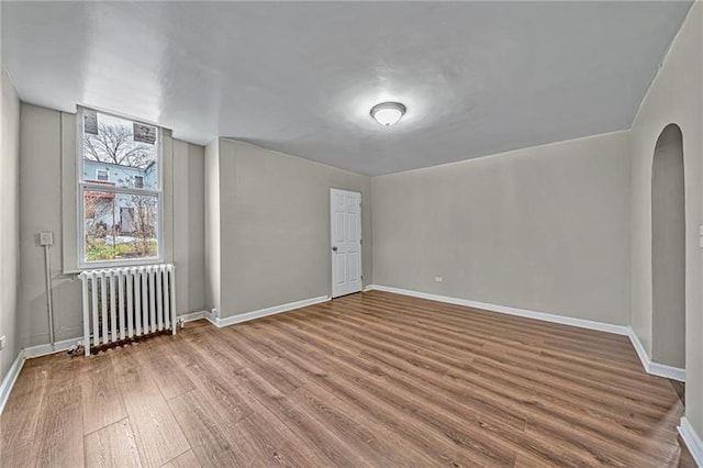 spare room featuring arched walkways, radiator, baseboards, and wood finished floors