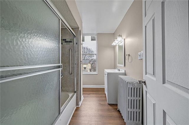 bathroom with wood finished floors, radiator heating unit, combined bath / shower with glass door, baseboards, and vanity