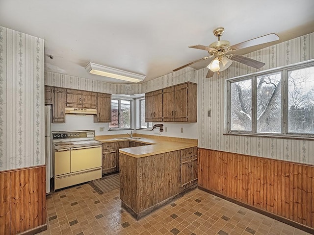 kitchen with sink, refrigerator, white range with electric cooktop, kitchen peninsula, and wood walls