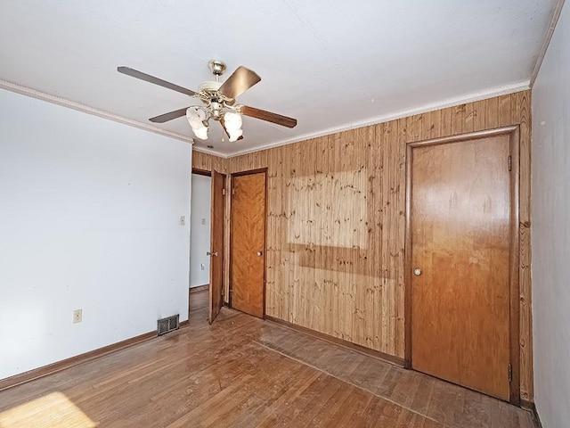 unfurnished bedroom featuring crown molding, ceiling fan, dark hardwood / wood-style flooring, and wood walls