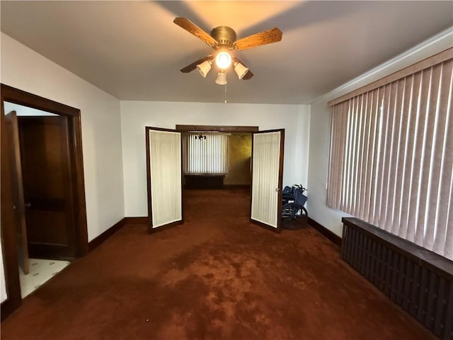 unfurnished bedroom featuring ceiling fan, radiator heating unit, and dark carpet