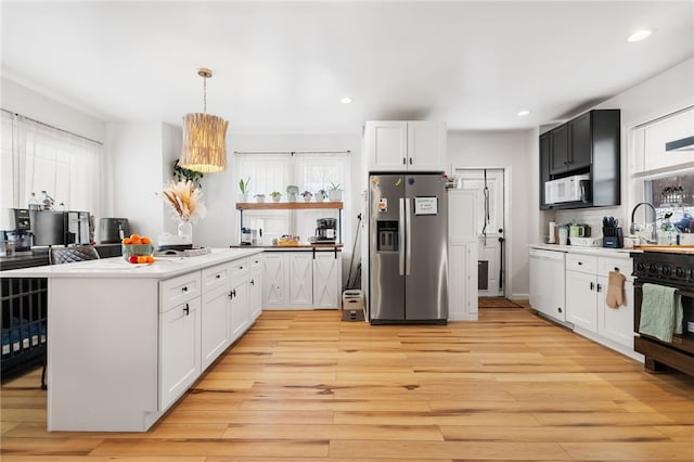 kitchen with sink, white appliances, white cabinetry, hanging light fixtures, and light wood-type flooring