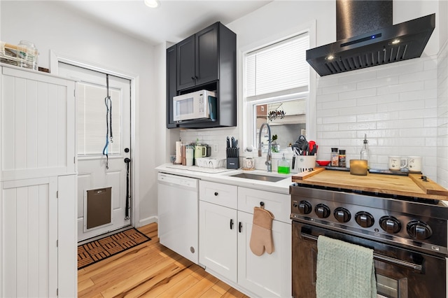 kitchen featuring wall chimney range hood, white appliances, sink, white cabinetry, and tasteful backsplash