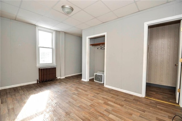 unfurnished bedroom with radiator, hardwood / wood-style floors, a drop ceiling, and a closet