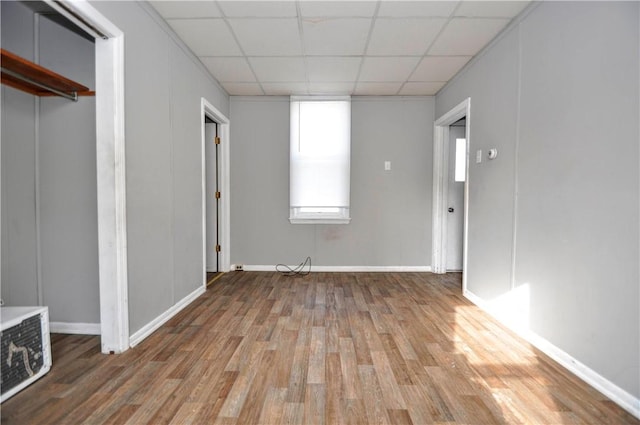 unfurnished bedroom featuring a paneled ceiling, a closet, and wood-type flooring