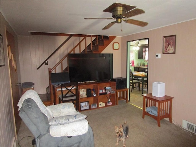 carpeted living room featuring wooden walls and ceiling fan