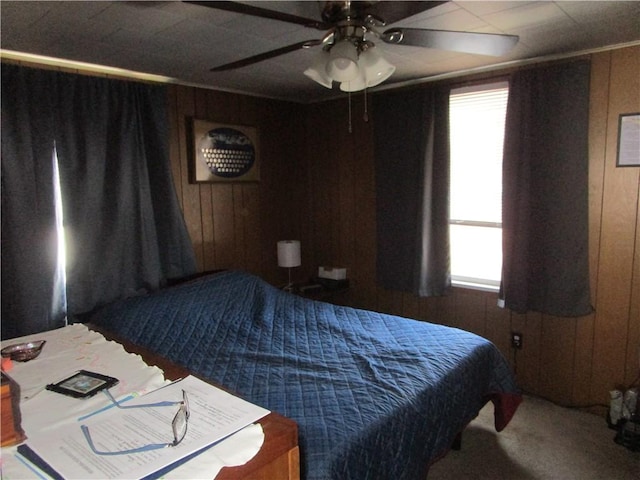 carpeted bedroom with multiple windows, ceiling fan, and wood walls