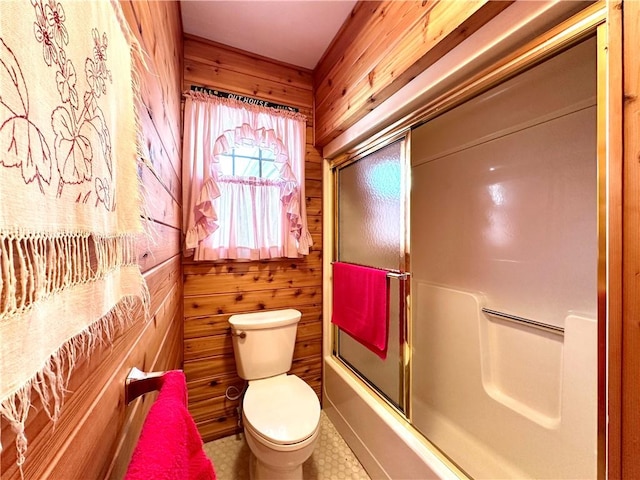 bathroom with toilet, shower / bath combination with glass door, and wood walls