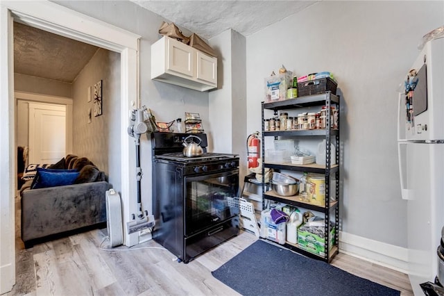 interior space featuring white refrigerator, white cabinets, light wood-type flooring, and black gas range