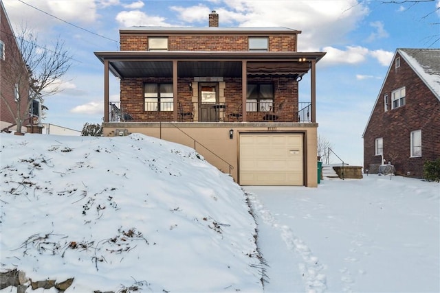 snow covered back of property featuring a porch and a garage