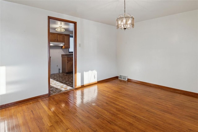 unfurnished room with an inviting chandelier and hardwood / wood-style floors