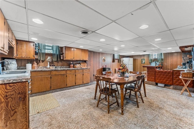 dining room with sink, a drop ceiling, and wooden walls