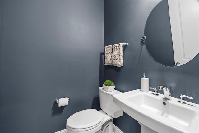 half bath with a sink, toilet, and baseboards