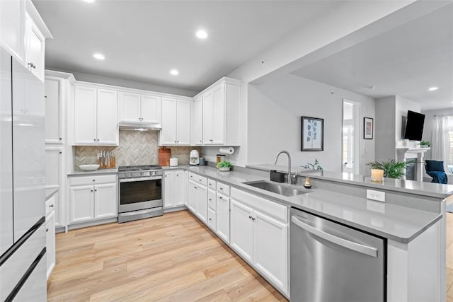 kitchen with a peninsula, appliances with stainless steel finishes, a sink, and white cabinetry