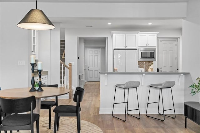 kitchen with light wood-style flooring, a peninsula, white cabinetry, freestanding refrigerator, and stainless steel microwave