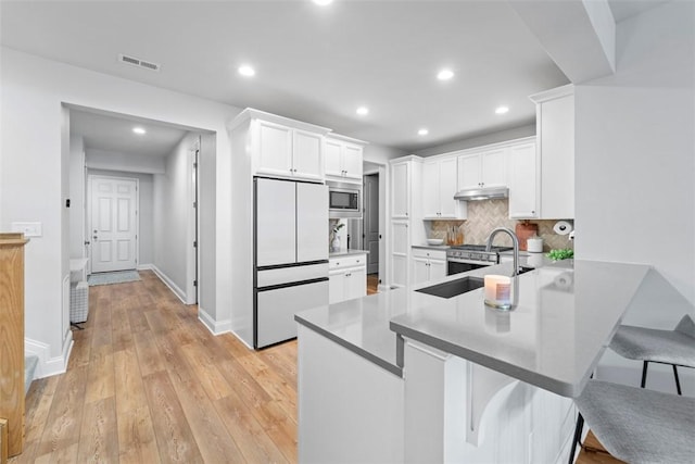 kitchen featuring white cabinets, appliances with stainless steel finishes, a kitchen breakfast bar, a peninsula, and under cabinet range hood