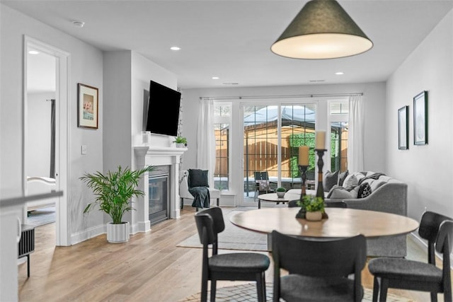 dining area with baseboards, light wood finished floors, a glass covered fireplace, and recessed lighting