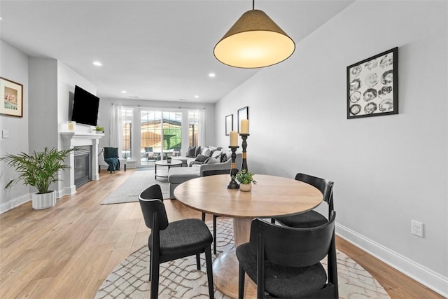 dining space featuring recessed lighting, light wood-type flooring, a glass covered fireplace, and baseboards