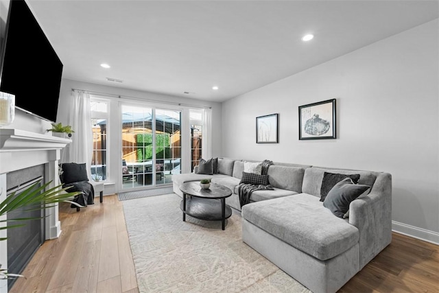 living room with recessed lighting, baseboards, wood finished floors, and a glass covered fireplace