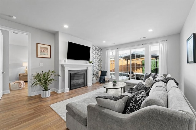 living room with light wood-type flooring, recessed lighting, baseboards, and a glass covered fireplace