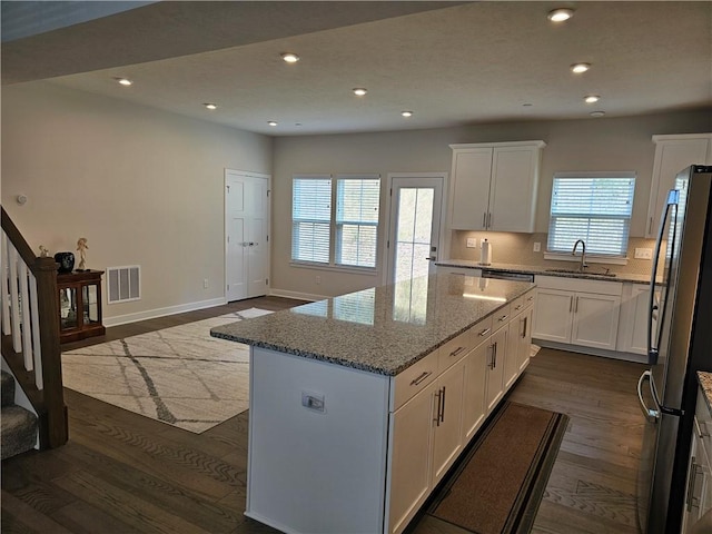 kitchen featuring light stone countertops, white cabinetry, a kitchen island, and stainless steel fridge