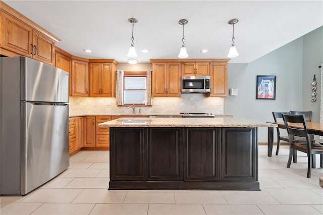 kitchen with pendant lighting, stainless steel appliances, a center island, and light stone countertops