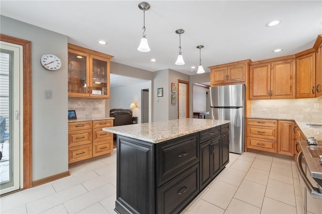 kitchen featuring stainless steel refrigerator, a center island, light stone counters, decorative backsplash, and decorative light fixtures